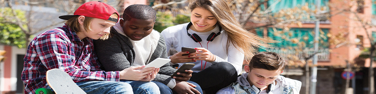 Positive teenage males and girls relaxing with mobile phones outdoor