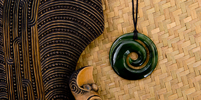 New Zealand - Maori themed objects - carved wooden mere and greenstone pendant on woven kite flax background